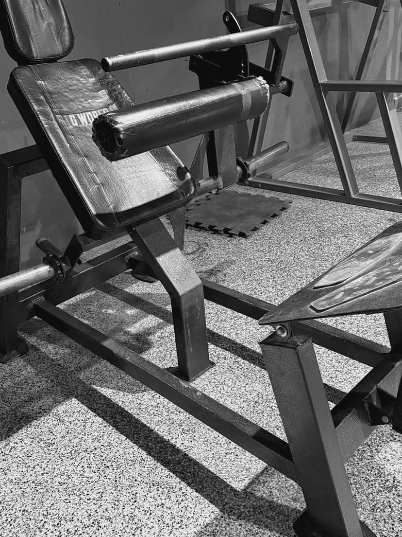 Máquina de hip thrust: respaldo acolchado inclinado, rodillo para apoyar sobre la cadera y plataforma para los pies.