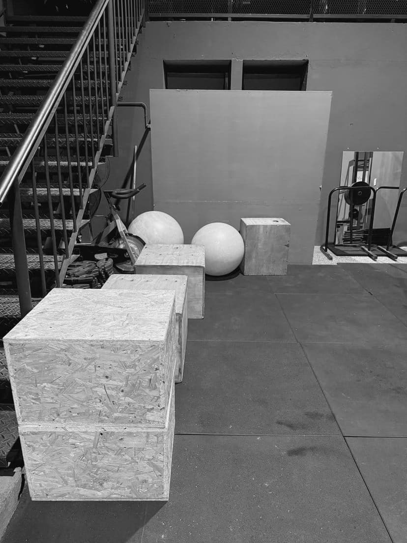 Cajones de madera para saltar, pelotas de pilates y una escalera metálica, con un rack al fondo.