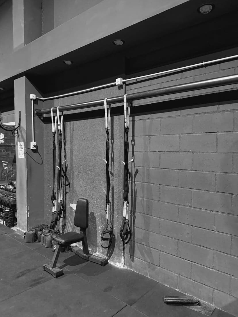 Correas de TRX colgadas de un caño en la pared, con un banco de apoyo al lado.